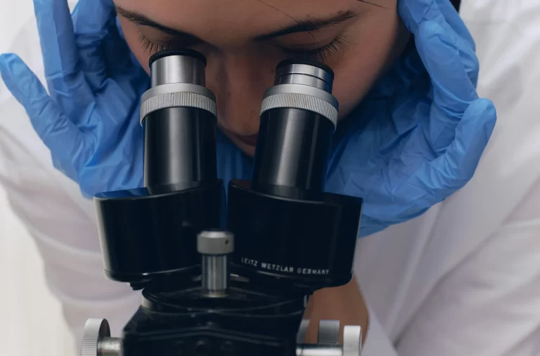 Cientista de luvas azuis observa uma amostra no microscópio