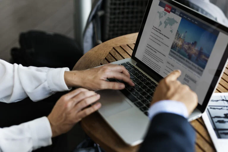 Duas pessoas trabalhando em notebooks com um site de notícias aberto