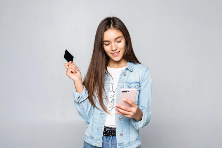 Jovem sorrindo, com o celular e um cartão de crédito nas mãos